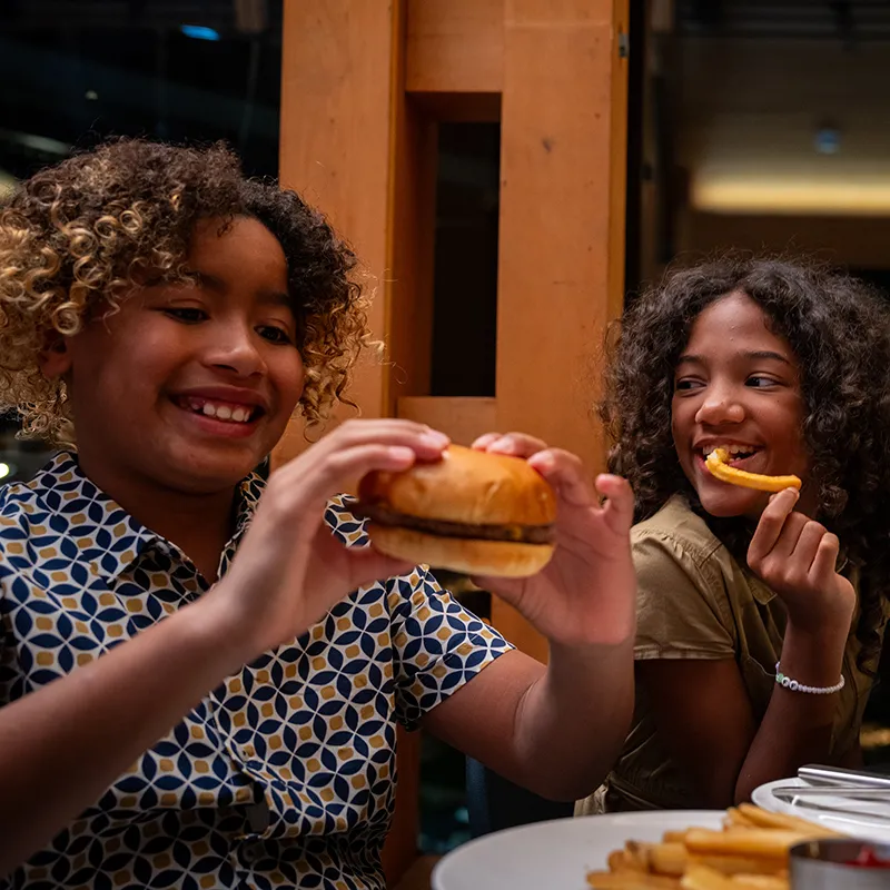 Kids Eating in Twin View An image of two kids smiling and enjoying their food while eating dinner in Twin View Restaurant and Bar at Evermore Orlando Resort.