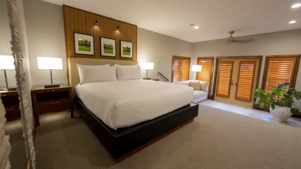 An image of an Evermore Orlando Resort Villa bedroom featuring a plush king-sized bed, a small step down towards a pull out couch and doors out to an exterior patio.